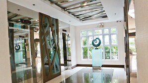 A spacious lobby with a modern ceiling design, large windows offering natural light, and a central art installation. - CondoDeal at Sea Residences (Pasay)