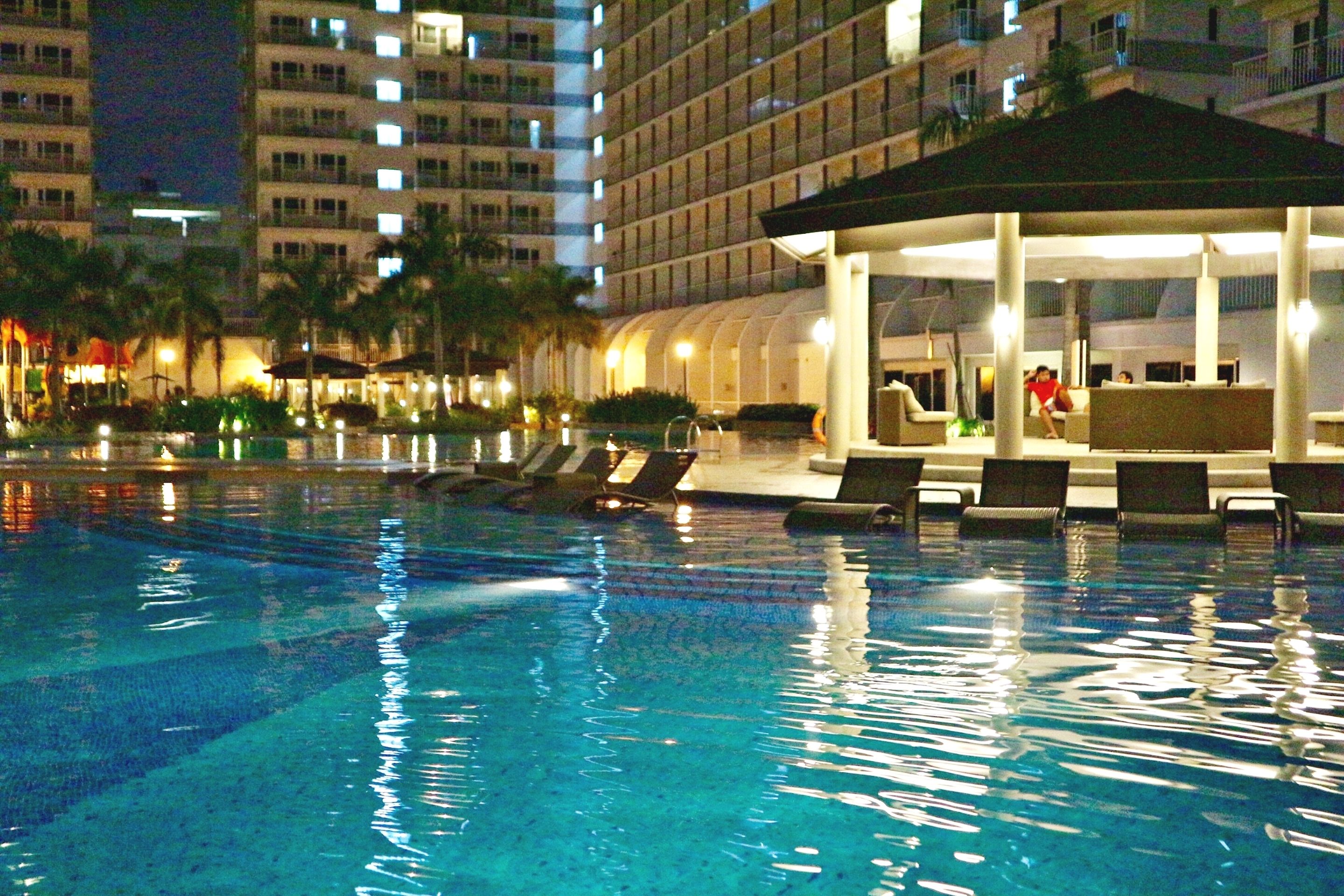 A swimming pool with lounge chairs and a covered seating area, surrounded by tall buildings.