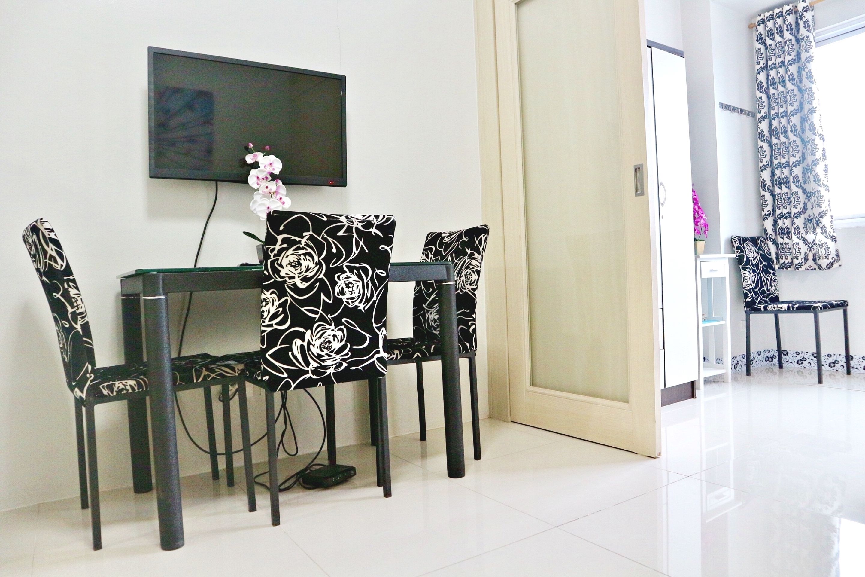 A dining area with a table and four chairs, a television mounted on the wall, and a door leading to another room.