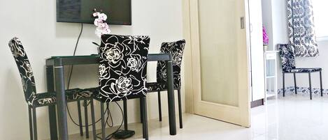 A dining area with a table and four chairs, a television mounted on the wall, and a door leading to another room.