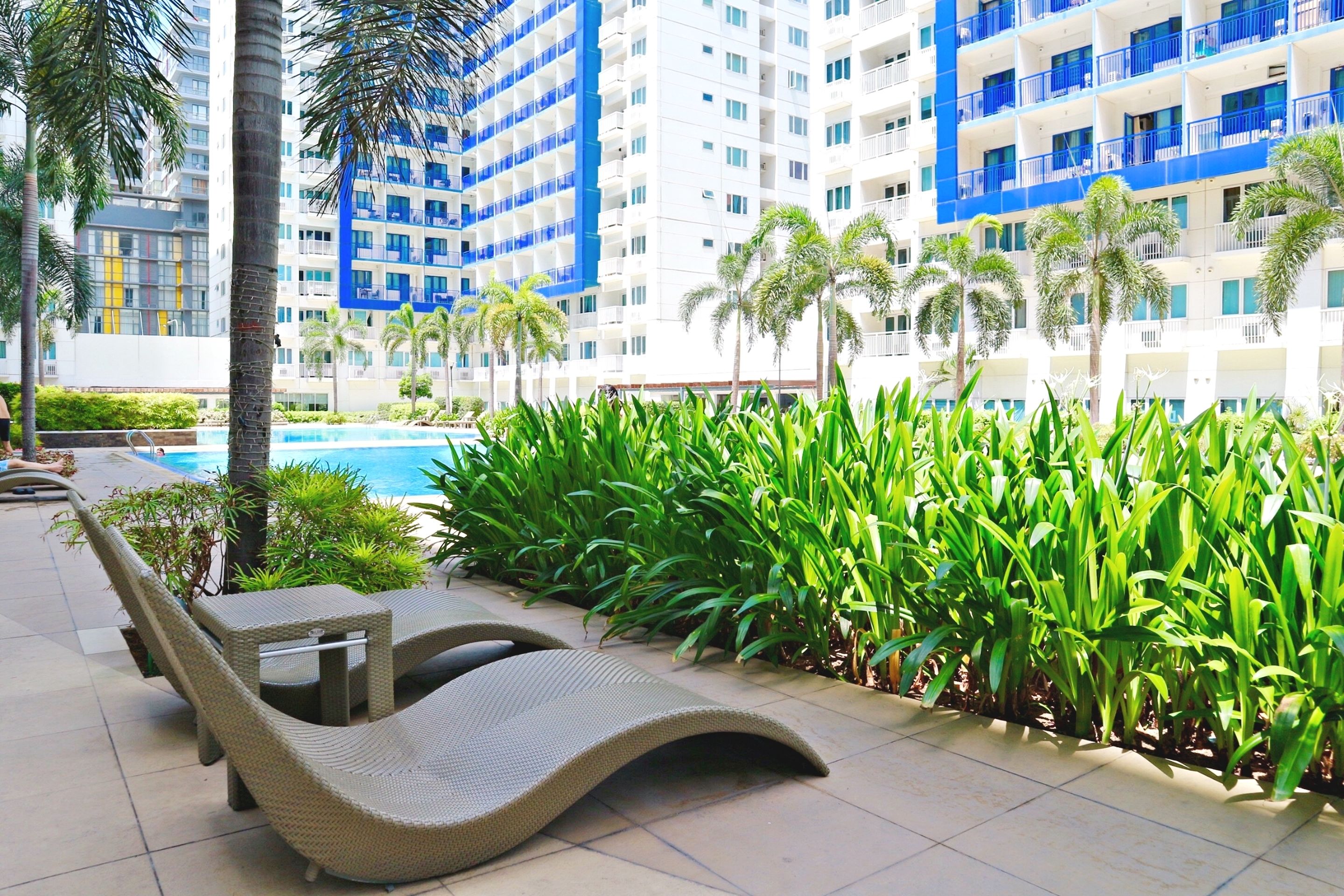 Zona junto a la piscina con sillones de descanso, una piscina y edificios altos al fondo.