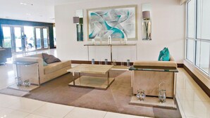 A modern lobby with a sofa, coffee table, and a large abstract painting. - CondoDeal at Sea Residences (Pasay)