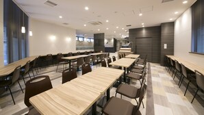 Une salle de conférence moderne, dotée de plusieurs tables et chaises, de grandes fenêtres équipées de stores et d’une palette de couleurs neutres.