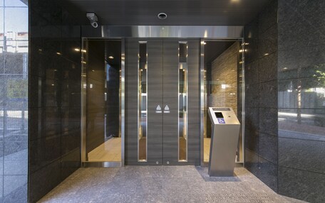 A modern elevator entrance with a metallic finish, glass panels, and a control panel.