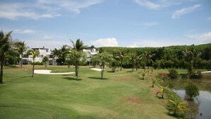 A golf course with a pond, palm trees, and a building in the background. - Phuket Apartment (Pa Klok)
