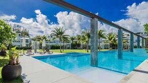 A swimming pool with a clear blue water, surrounded by palm trees and lounge chairs. - Phuket Apartment (Pa Klok)
