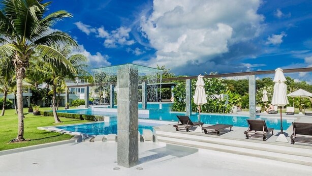 A pool area with lounge chairs and umbrellas, surrounded by palm trees and a clear sky. - Phuket Apartment (Pa Klok)