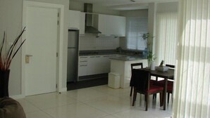 A modern kitchen with white cabinets, a built-in oven, and a dining area with a table and chairs. - Phuket Apartment (Pa Klok)