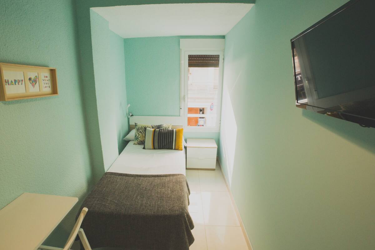 Una habitación pequeña y funcional con cama, escritorio y televisión.