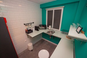 Cocina compacta con paredes blancas y turquesa, una encimera blanca, un lavamanos, un microondas y un pequeño cubo de basura.