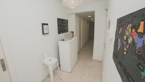Een hal met een receptiebalie, een witte stoel, een laptop, een wereldkaart en een deur naar een andere kamer.