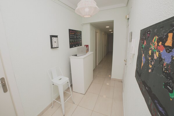 Un pasillo con una recepción, una silla blanca, una computadora portátil, un mapa mundial y una puerta que da a otra habitación.