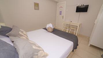 Un dormitorio con cama, almohadas, una mesita de noche, una silla y un televisor en la pared.
