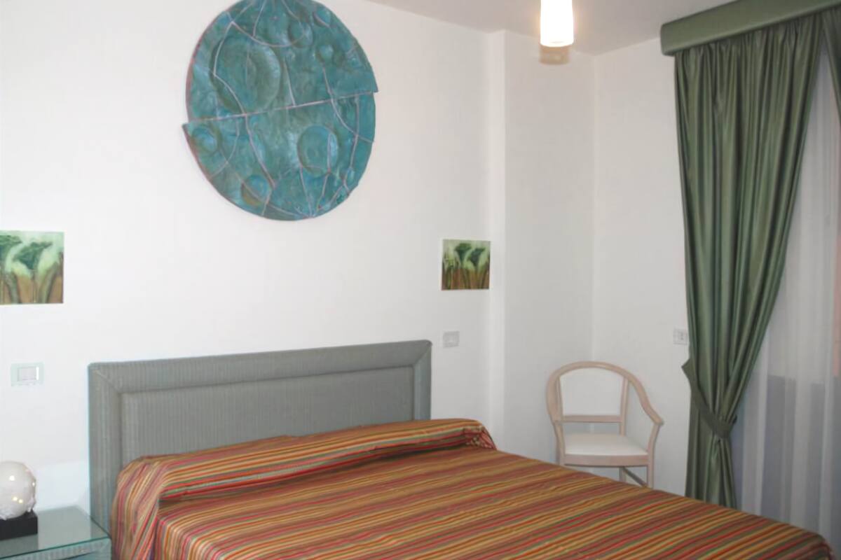 A bedroom with a bed, a chair, a round wall decoration, and a window with curtains.