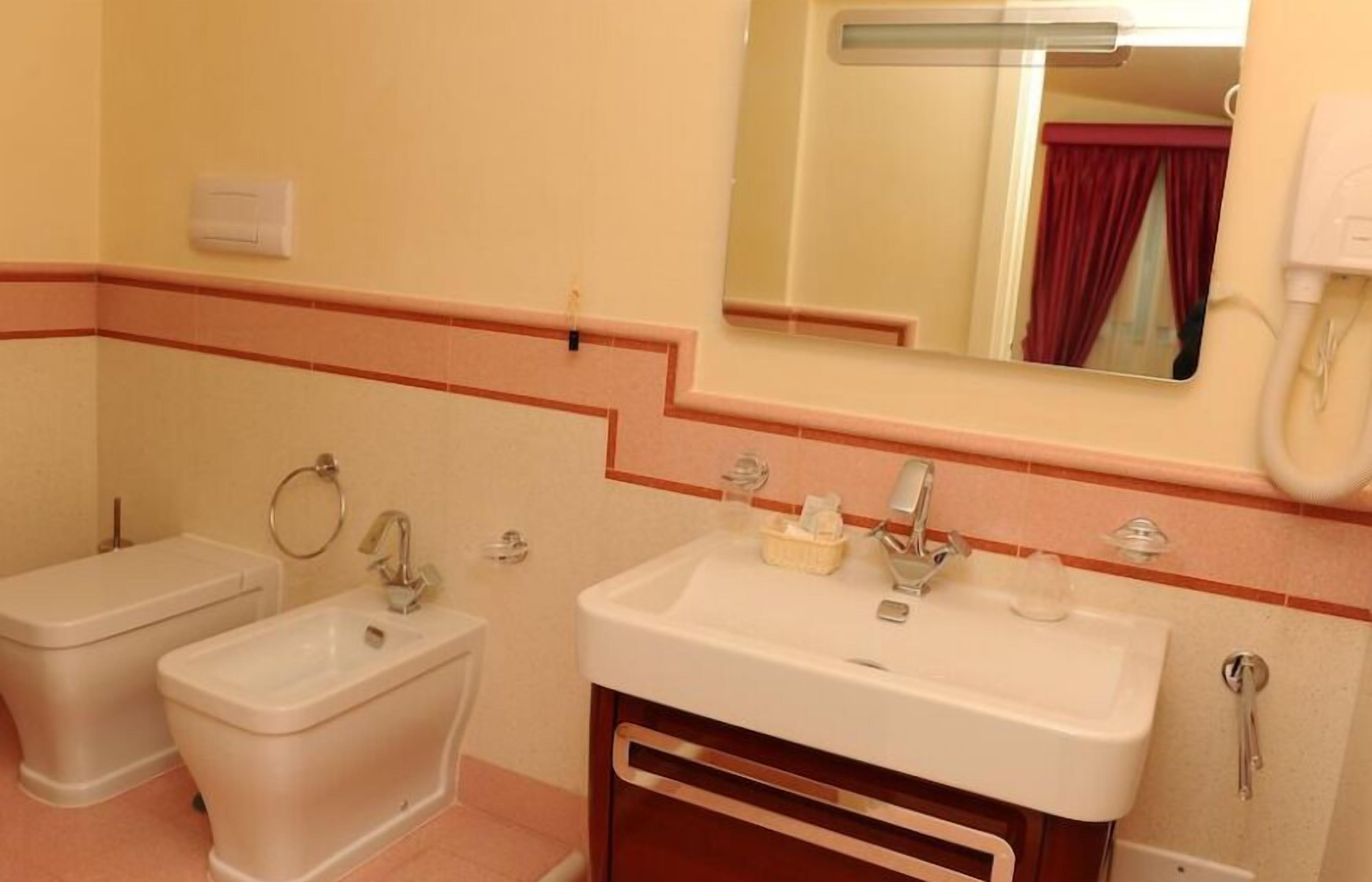 Een badkamer met twee toiletten, een wastafel, een spiegel en een handdoekhouder.