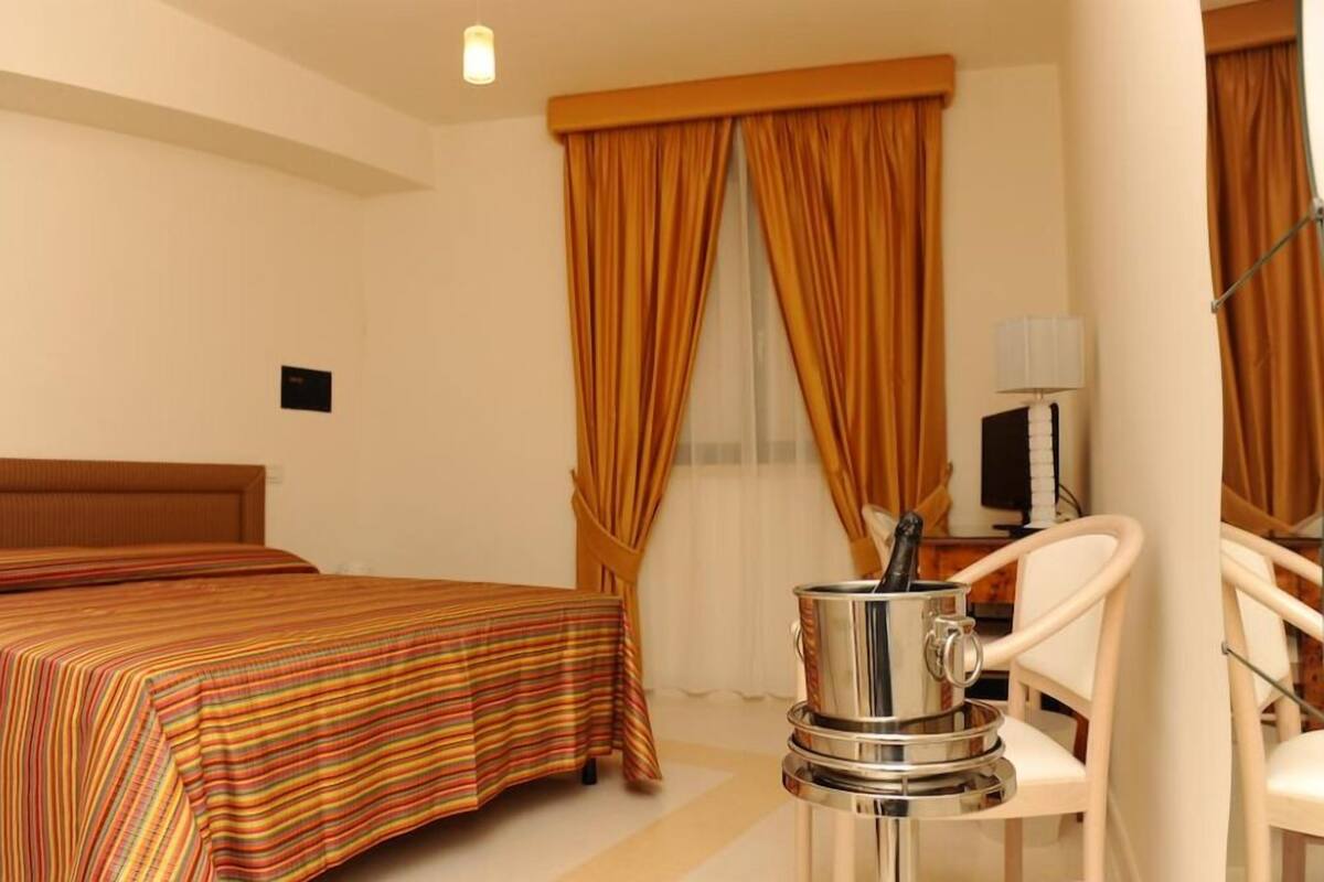 A hotel room with a bed, a chair, a coffee machine, and curtains.
