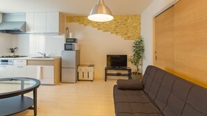 A modern kitchen with white cabinets, a built-in stove, and a microwave. There's a dining table with chairs, a sofa, and a TV on a stand. - Grandouce Namba-Nishi (Osaka)