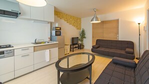 A modern kitchen with white cabinets, a dining table, and a sofa in a living area. - Grandouce Namba-Nishi (Osaka)