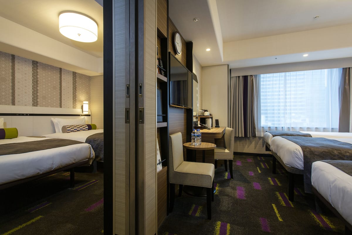 A hotel room with two beds, a desk, a chair, a clock, and a window with curtains.