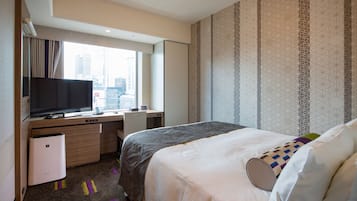 A hotel room with a bed, a desk, a television, and a window with a city view.