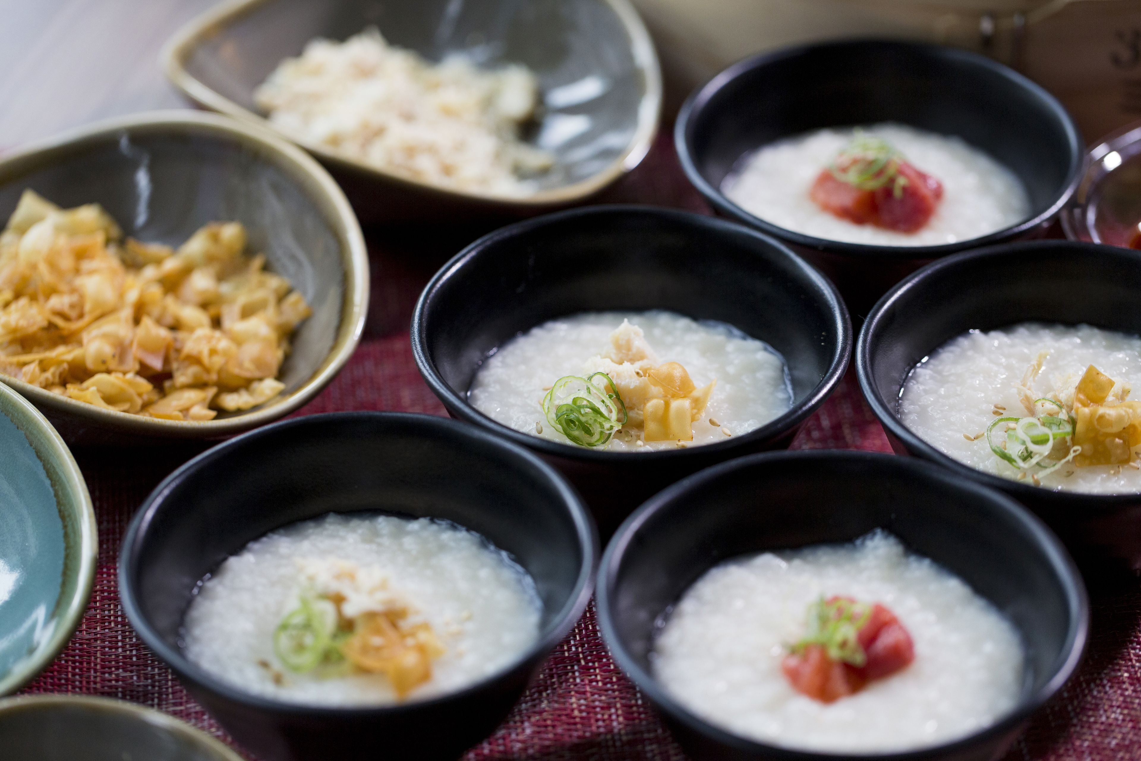 Bowls of rice porridge with toppings, arranged on a table.
