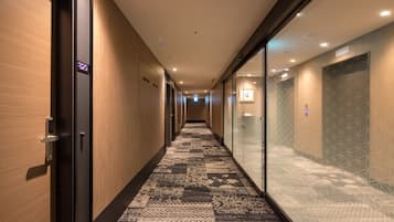 A hotel hallway with wooden walls, a patterned carpet, and glass doors leading to rooms.