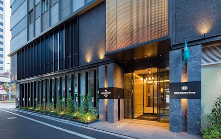 A modern hotel entrance with a glass facade, a sign for Hotel Monterrey Group, and a well-lit entrance area.