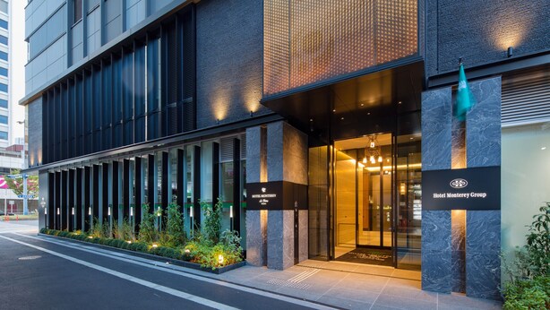 Una entrada moderna de hotel con fachada de vidrio, un letrero de Hotel Monterrey Group y un área de acceso bien iluminada.