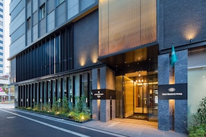 A modern hotel entrance with a glass facade, a sign for Hotel Monterrey Group, and a well-lit entrance area.