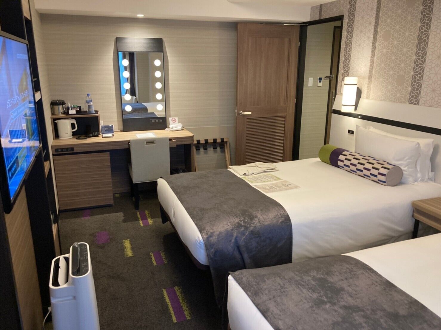 Una habitación de hotel con cama, escritorio con espejo, televisor y minibar.