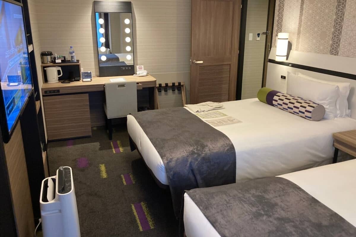 A hotel room with a bed, a desk with a mirror, a television, and a minibar.