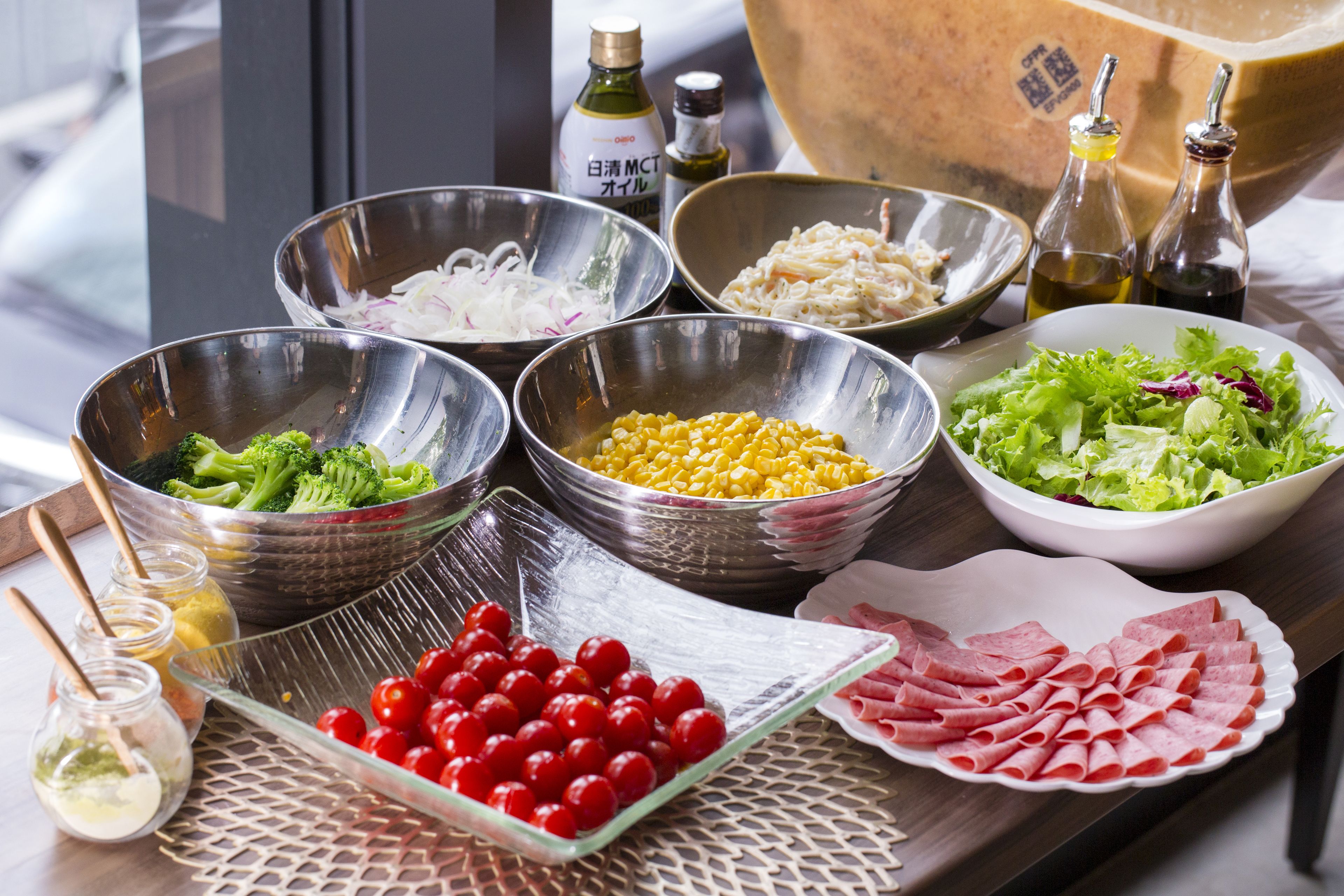 A table with various food items and condiments, including bowls of vegetables, corn, and a plate of sliced meat.