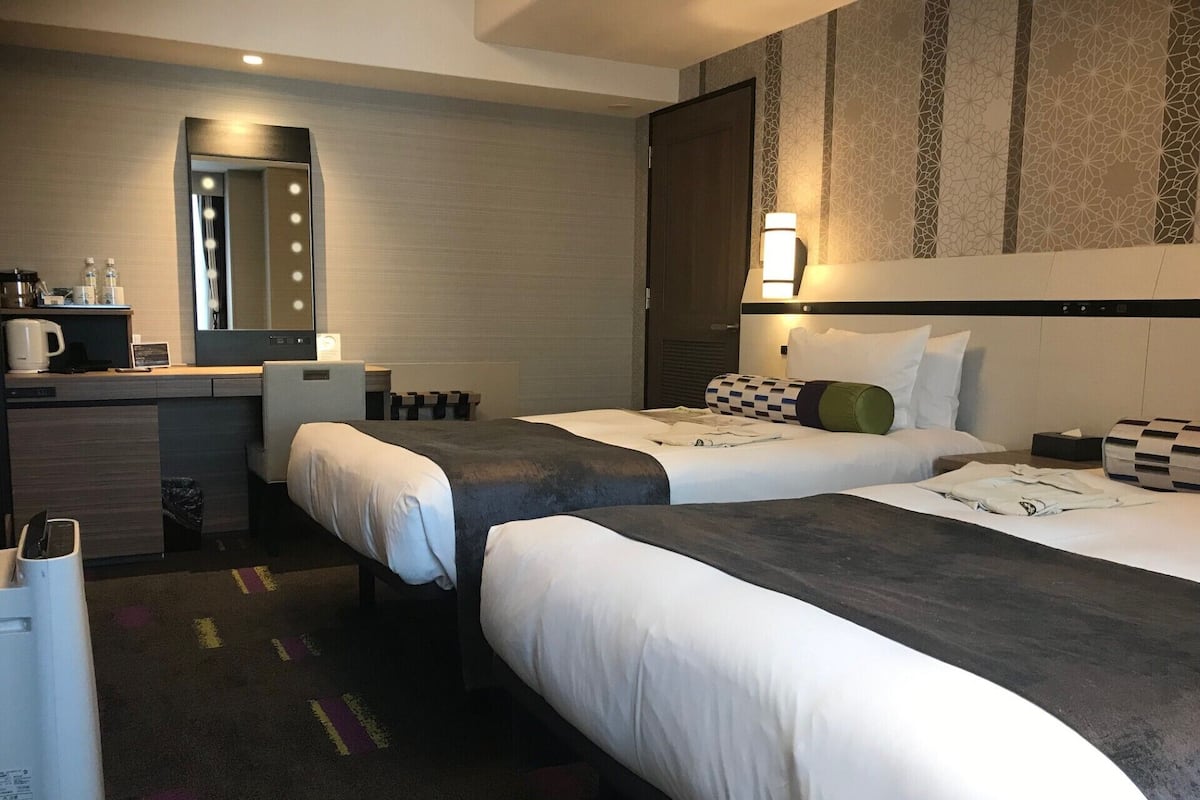 A hotel room with two beds, a desk with a coffee maker, a mirror, and a patterned wall.