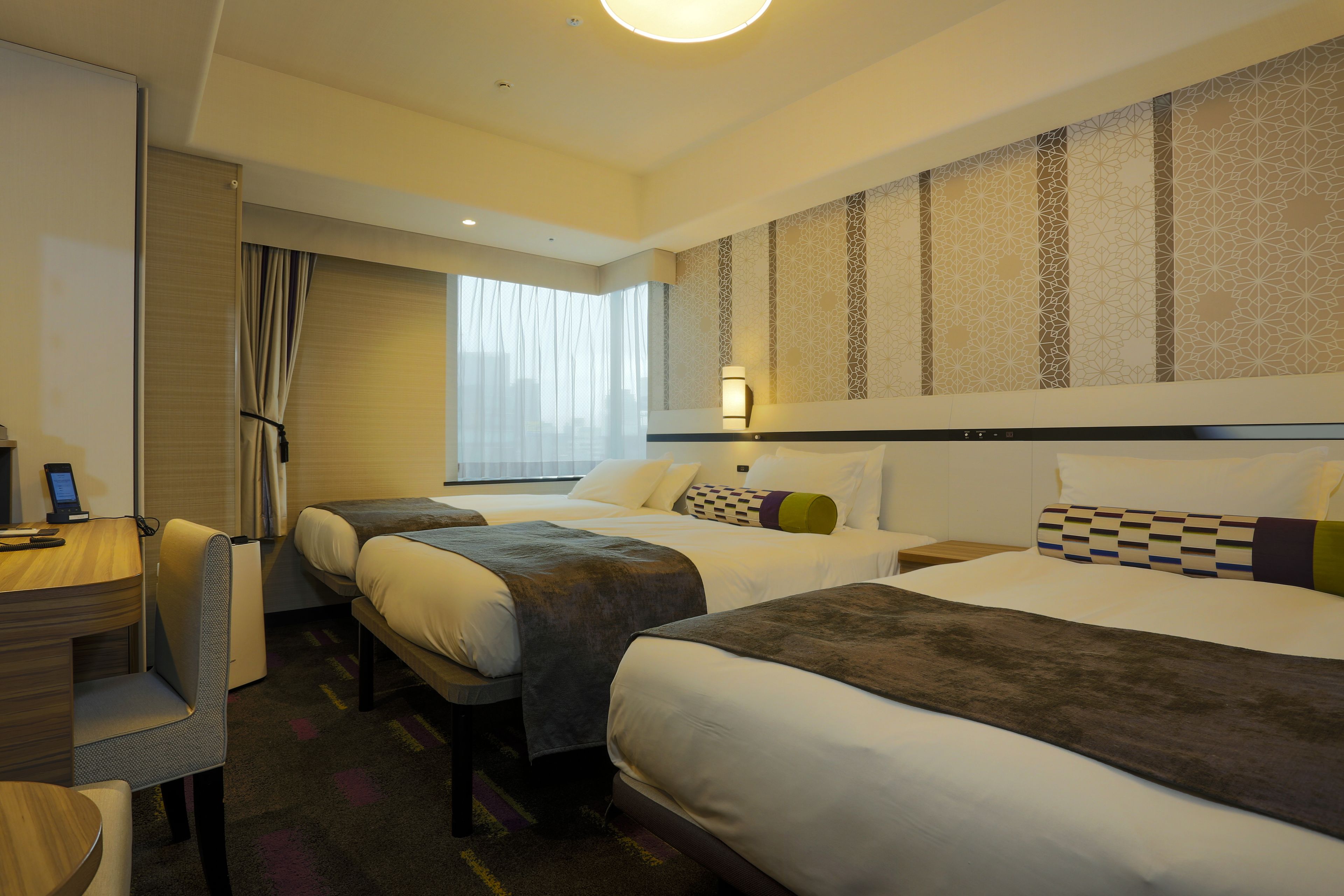 Quarto de hotel com duas camas, uma escrivaninha e uma cadeira.