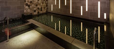 Un moderno espacio de spa con suelo a cuadros, piscina de cristal y pared con luminarias geométricas.