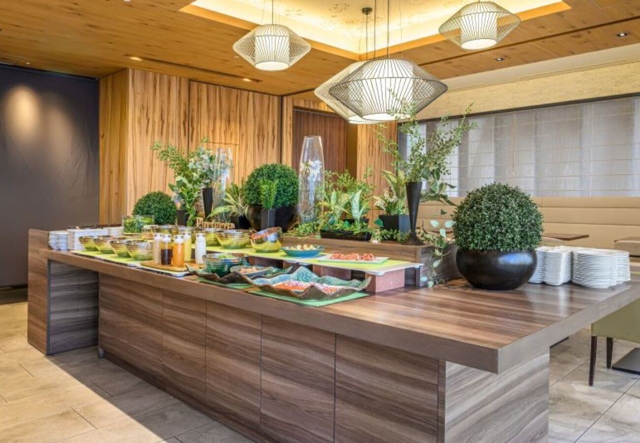 Un área de recepción moderna con un mostrador de madera, plantas en macetas y una mesa de buffet.