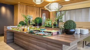 Un área de recepción moderna con un mostrador de madera, plantas en macetas y una mesa de buffet.