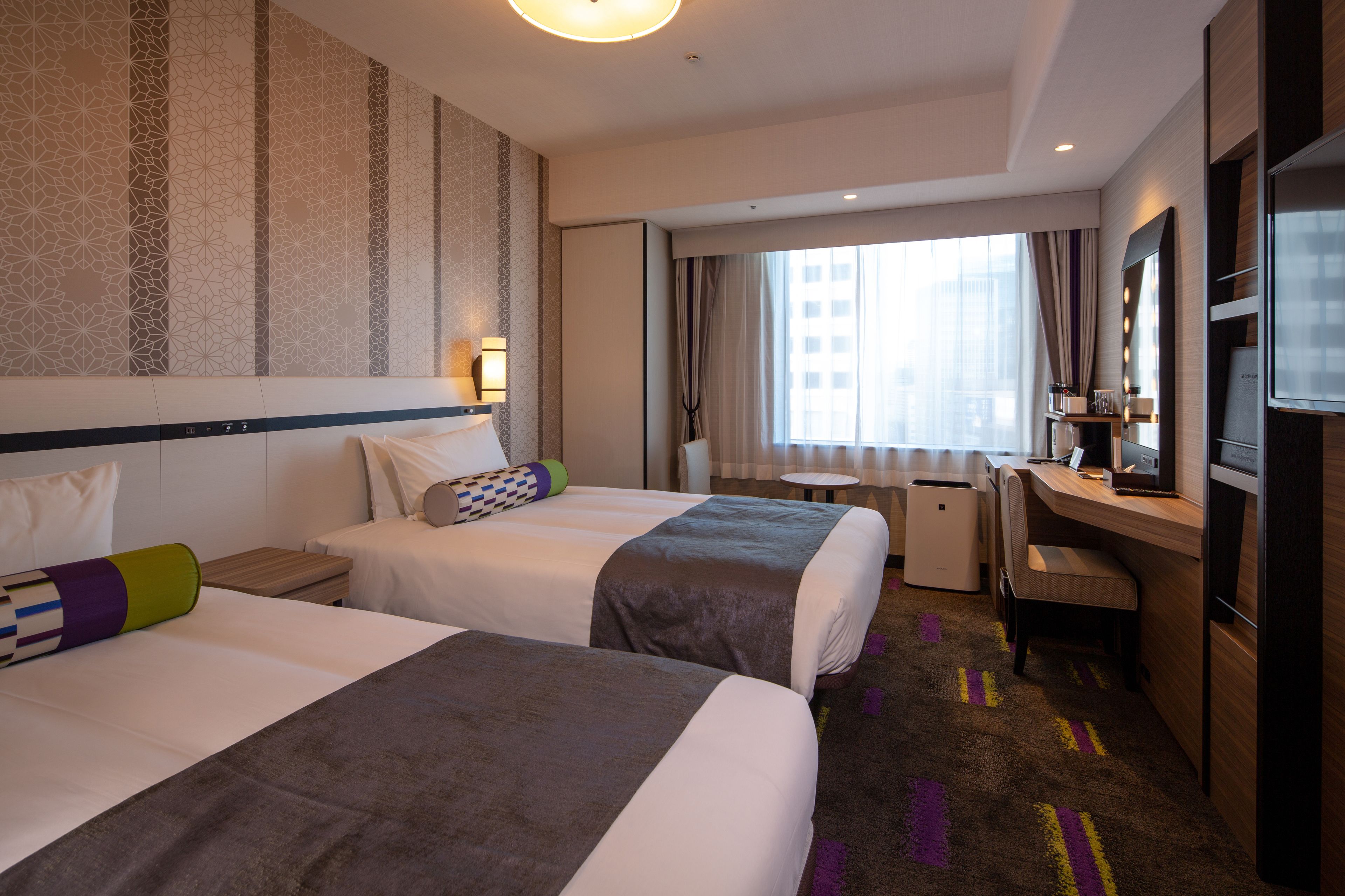 A hotel room with two beds, a desk, a chair, a TV, and a window with curtains.