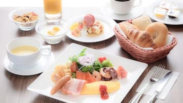 A breakfast setting with croissants, a plate of assorted food, a glass of orange juice, and a cup of coffee.