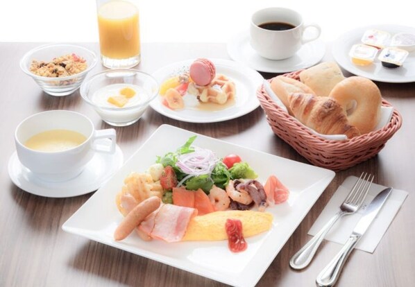 Un desayuno con cruasanes, un plato de comida variada, un vaso de zumo de naranja y una taza de café.