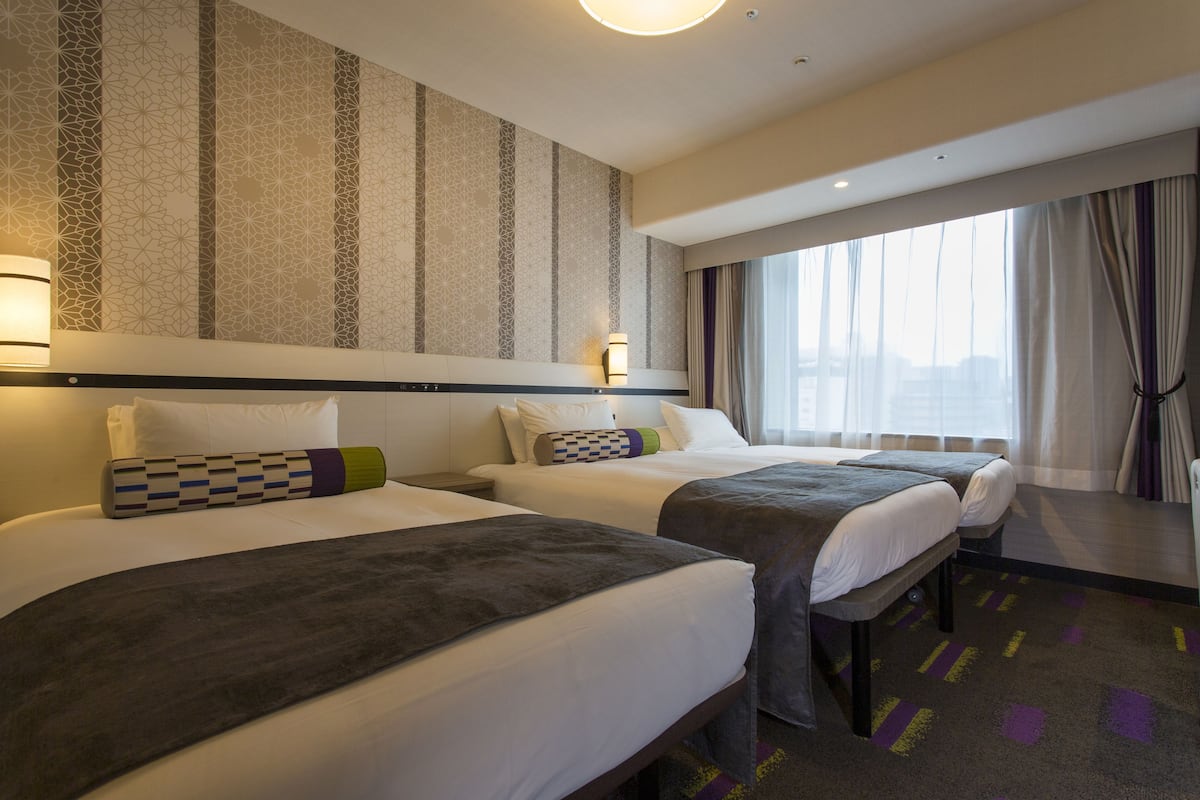 A hotel room with two beds, a large window with curtains, and a patterned wall.