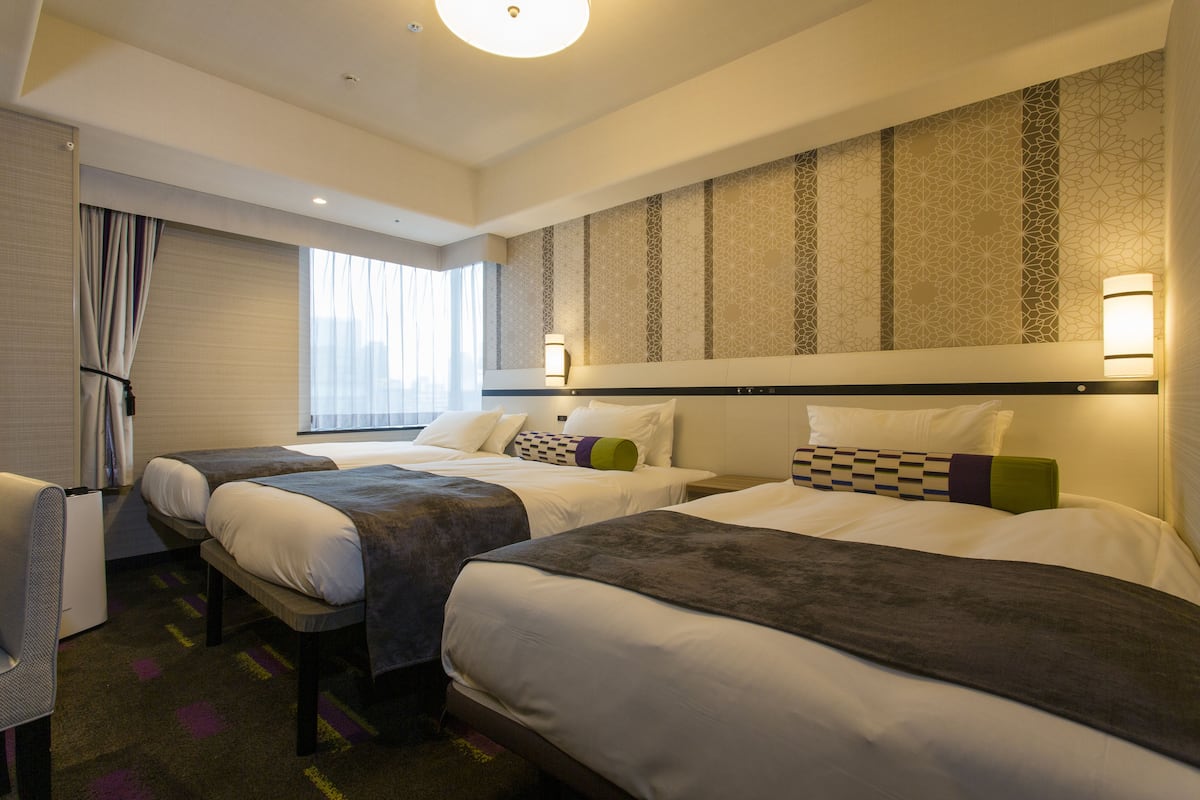 A hotel room with two beds, a desk, and a window with curtains.