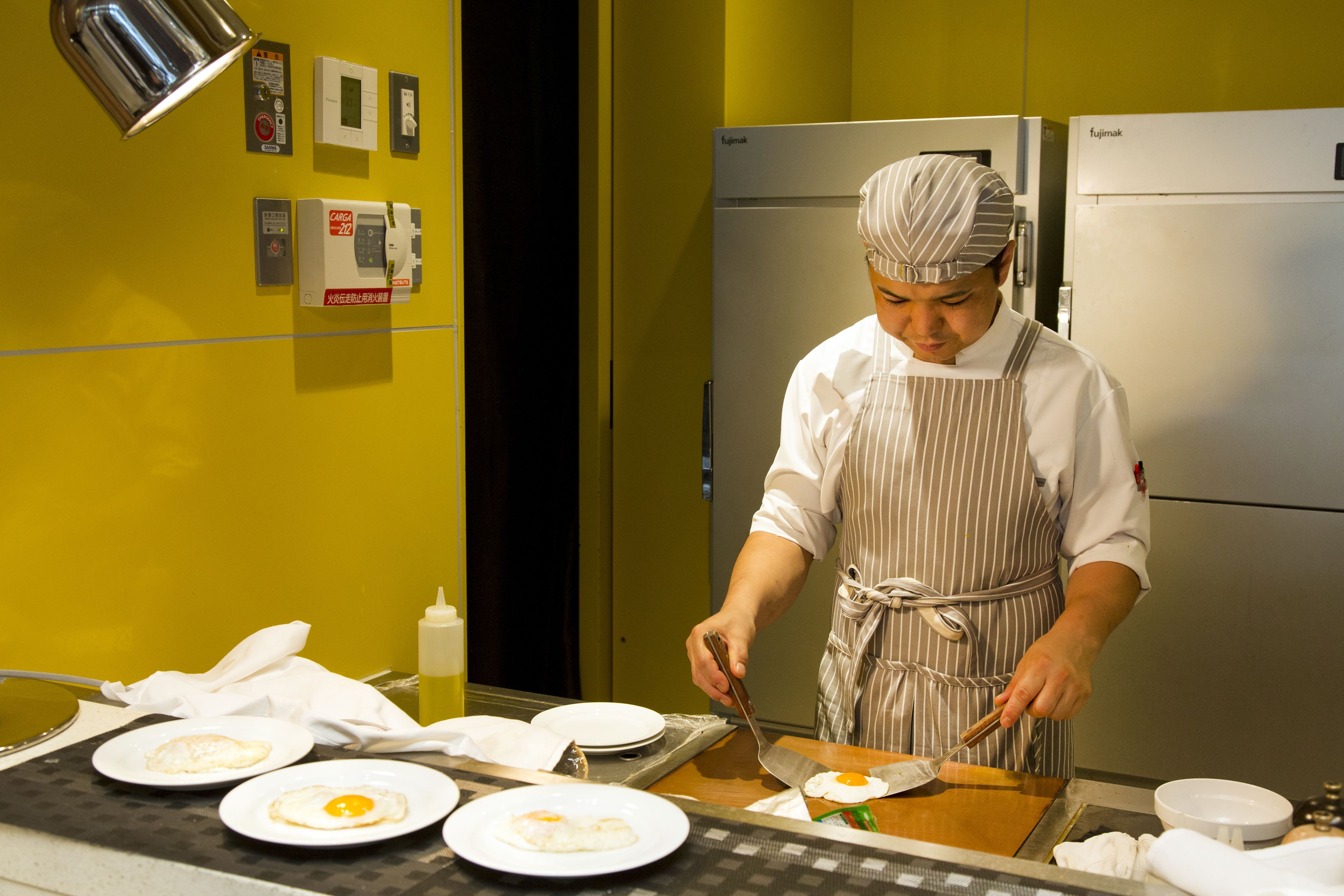 A chef preparing food in a kitchen with a refrigerator and various appliances.