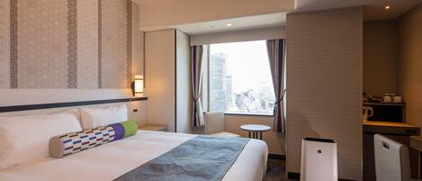 A hotel room with a large bed, a desk, a chair, a small table, and a view of the city through the window.