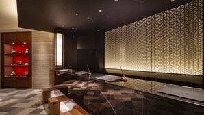Un área de recepción moderna con una pared de diseño geométrico, un mostrador de recepción y una unidad de estanterías de madera con plantas.