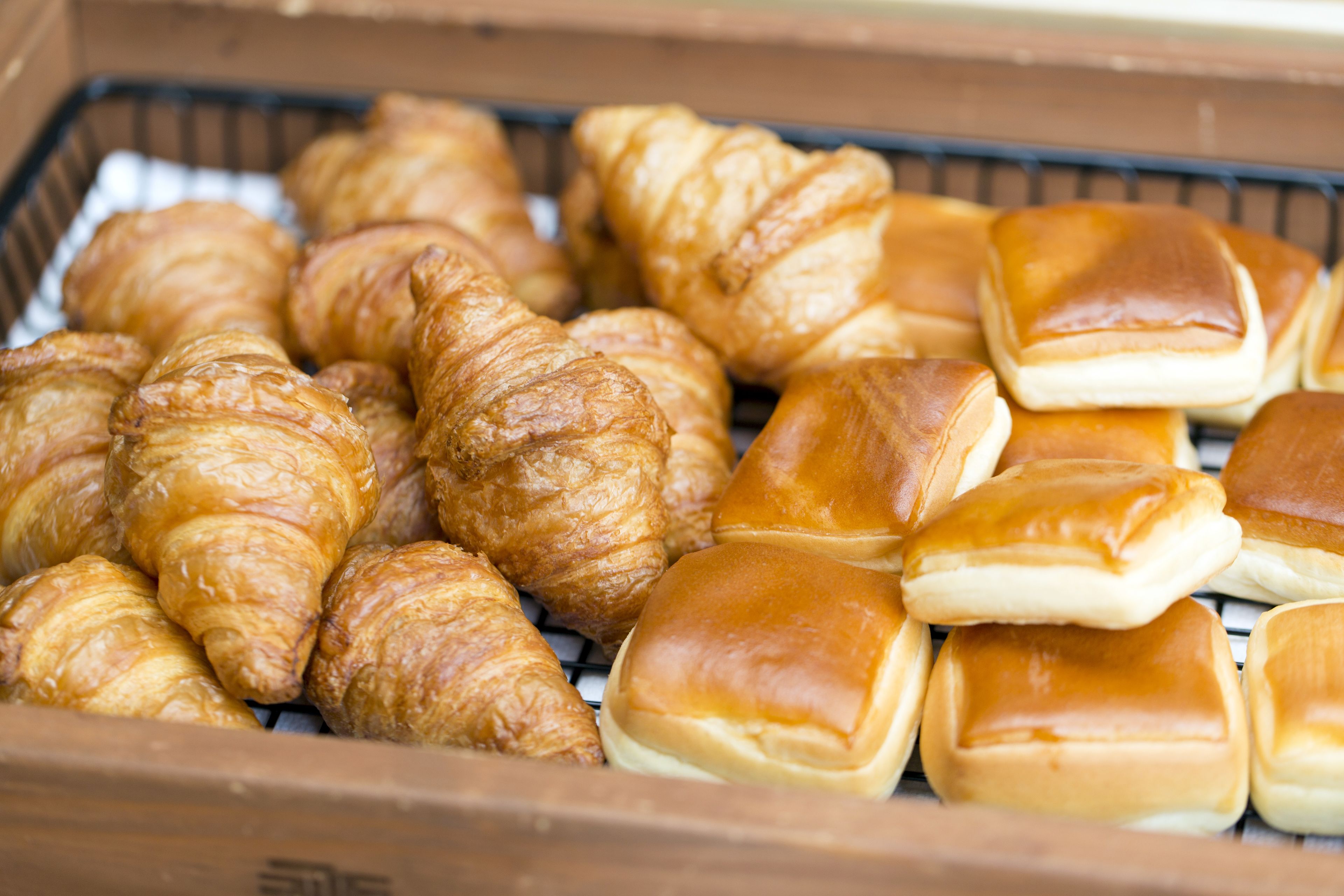 A wooden box containing various baked goods, including croissants and rolls.