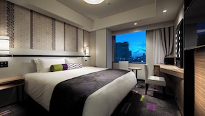 Una habitación de hotel moderna con una cama grande, un escritorio, una silla y vistas a un paisaje urbano de noche.