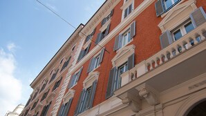 A multi-story building with a red facade, white trim, and blue shutters. - Affitta Camere Via Veneto (Rome)