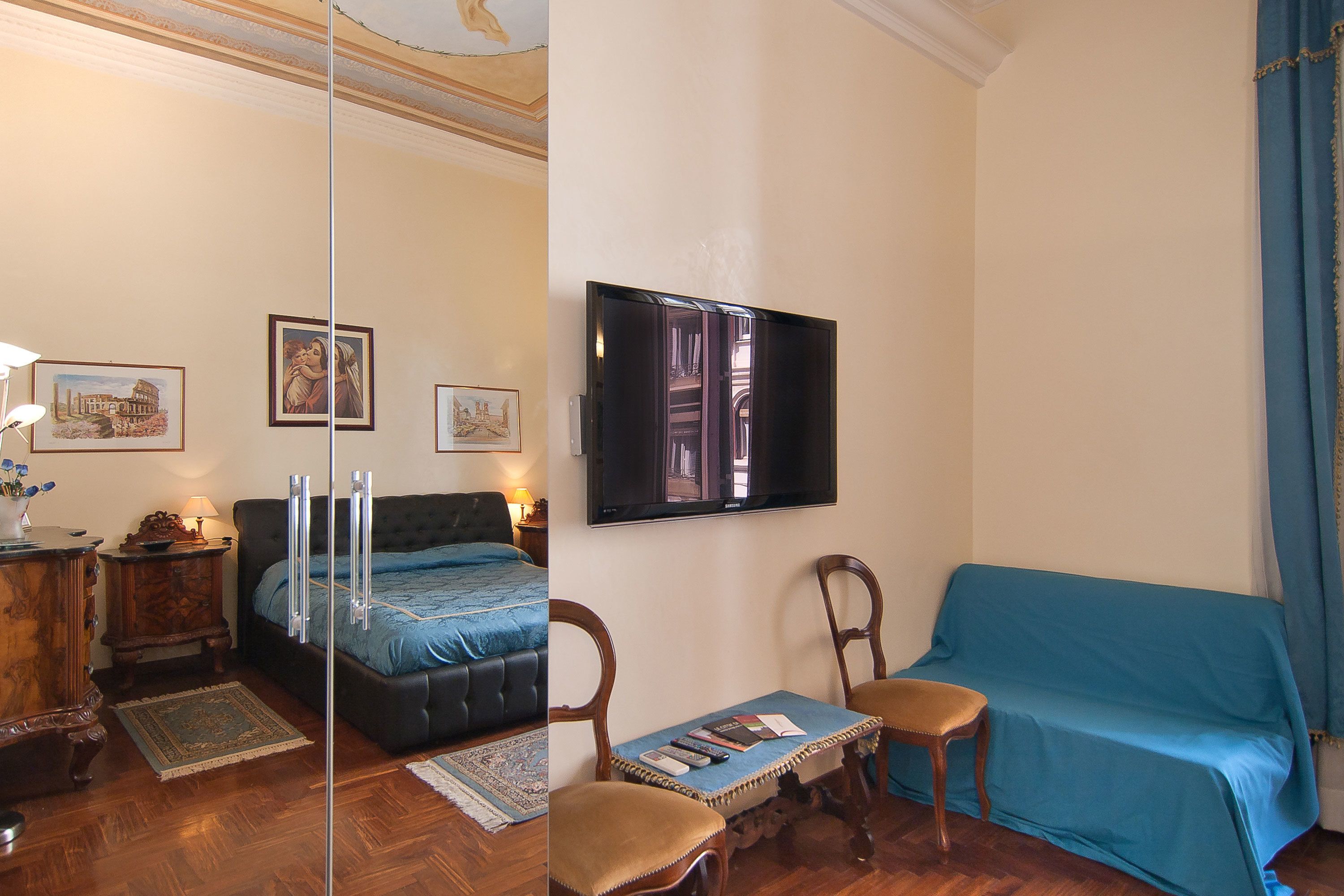 A bedroom with a bed, a TV, a sofa, and a chair.