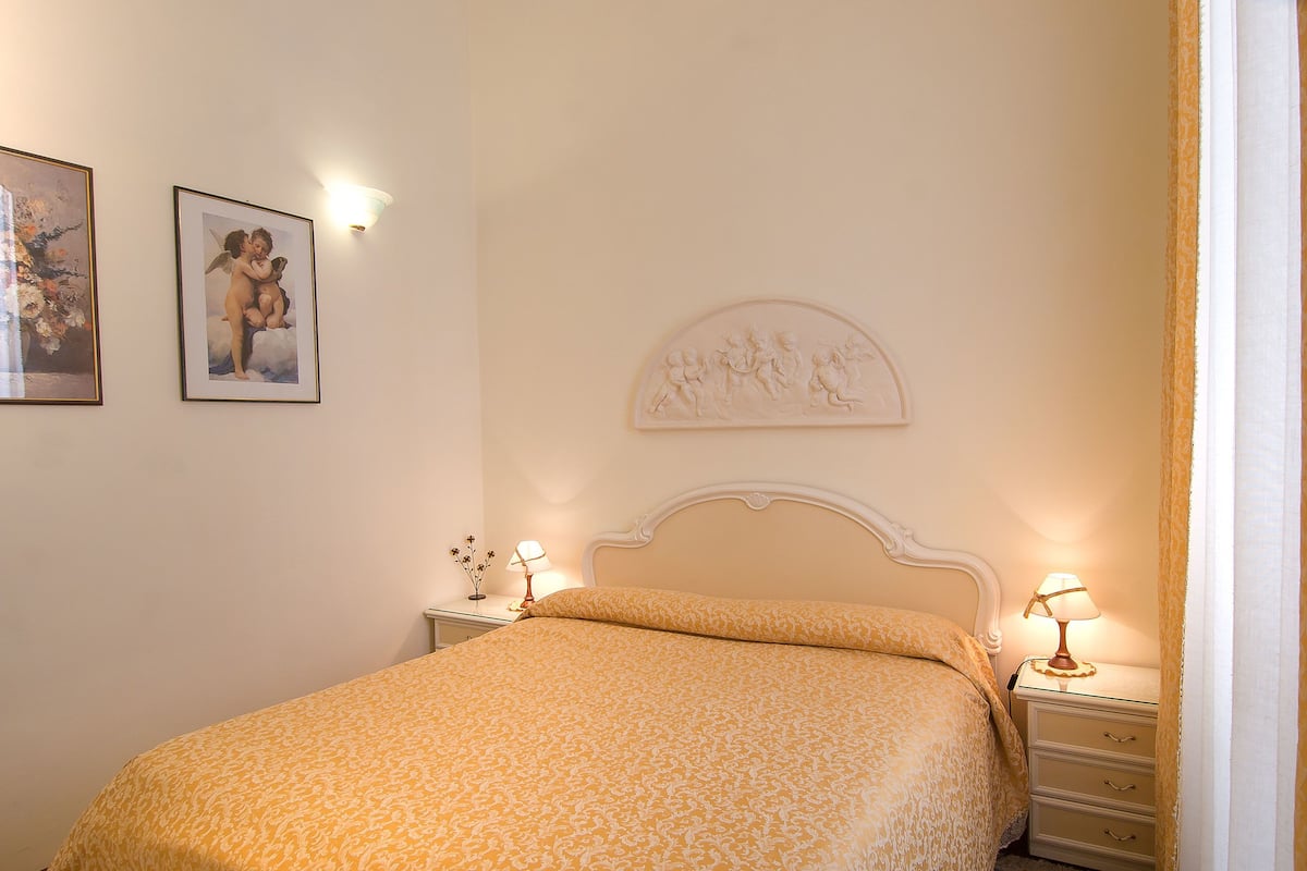 A neatly made bed with a patterned bedspread, a nightstand with a lamp, and wall art.